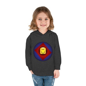 K&ouml;nnte beinhalten: Ein dunkelgrauer Kapuzenpullover mit einem blauen und roten Kreis-Motiv, das ein gelbes Smiley-Gesicht in einem roten Diamanten zeigt. Der Pullover ist f&uuml;r Kinder konzipiert.