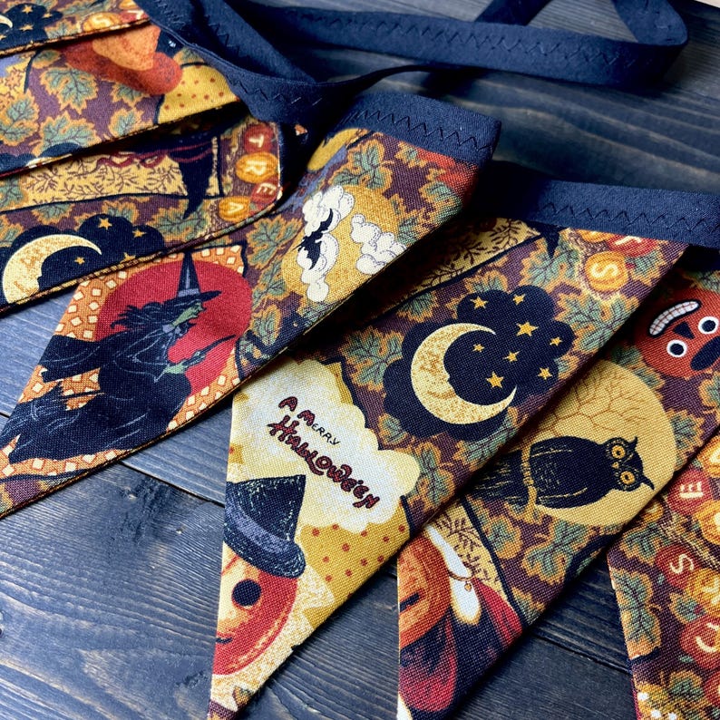 May include: A Halloween-themed banner with various festive designs. The pennants feature images of a witch, owl, moon, and pumpkin, along with the text "A Merry Halloween." The banner is made of fabric with a dark blue trim and a matching ribbon.