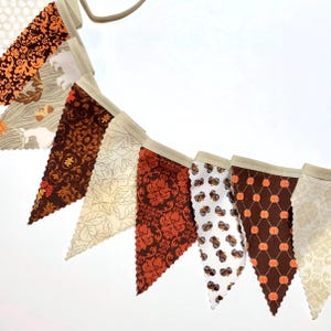 May include: A fall-themed fabric banner with alternating brown, orange, and white triangular flags. Each flag features a different pattern, including acorns, pumpkins, and leaves.