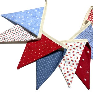 Peut inclure: Une guirlande de fanions festive avec des drapeaux triangulaires altern&eacute;s. Les drapeaux pr&eacute;sentent des motifs d'&eacute;toiles blanches sur fond bleu, rouge et bleu, et de petites fleurs rouges sur fond blanc. La guirlande est enfil&eacute;e sur un ruban de couleur naturelle.