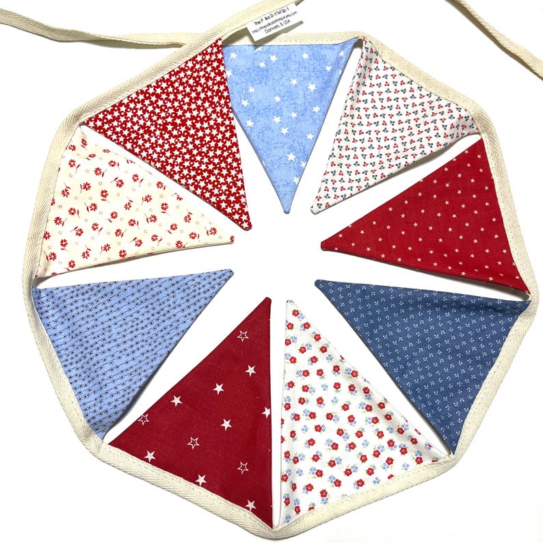 Peut inclure: Guirlande de fanions circulaires avec des drapeaux triangulaires rouges, blancs et bleus altern&eacute;s. Les drapeaux pr&eacute;sentent des motifs d'&eacute;toiles et de fleurs, et sont bord&eacute;s d'un tissu cr&egrave;me. Un ruban cr&egrave;me est attach&eacute; pour l'accrochage.