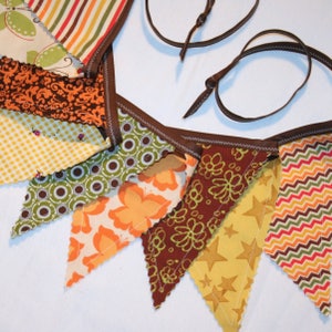 May include: A brown fabric banner with a scalloped edge and a variety of patterned fabric triangles. The triangles feature different patterns, including polka dots, butterflies, and zigzags. The banner is strung with brown cord.