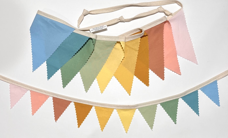 Puede incluir: Una pancarta de tela colorida con banderas triangulares en tonos de azul, verde, amarillo, naranja y rosa. La pancarta est&aacute; enhebrada en un cord&oacute;n blanco y tiene un borde festoneado.