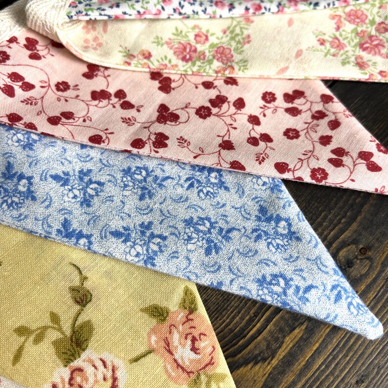 May include: Close-up of several fabric swatches with floral patterns. The fabrics feature various colors, including pink, blue, and yellow, with designs of roses and other flowers. The swatches are arranged on a wooden surface.