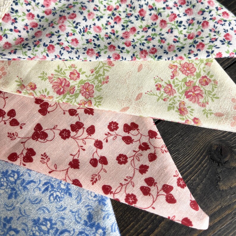 May include: Close-up of four fabric swatches with floral patterns. The fabrics feature a variety of colors, including pink, red, blue, and cream. The patterns include small flowers and vines, creating a vintage aesthetic.