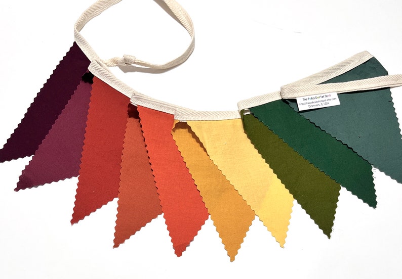 K&ouml;nnte beinhalten: Ein Stoffbanner mit zehn dreieckigen Flaggen in den Farben Burgunderrot, Orange, Gelb und Gr&uuml;n. Die Flaggen sind mit wei&szlig;em Stoff zusammengen&auml;ht und haben eine wei&szlig;e Schnur zum Aufh&auml;ngen.