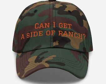 Puede incluir: Gorra de béisbol de camuflaje con el texto "CAN I GET A SIDE OF RANCH?" en naranja. La gorra presenta un diseño clásico de seis paneles, una visera curva y una correa ajustable en la parte trasera.