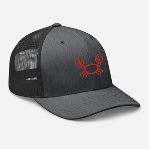 May include: A dark gray and black trucker hat with a red embroidered crab design.