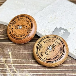 May include: Two circular wooden bread lame handles with engraved designs. One shows a loaf, the other a baguette. Both have the names "Jordan & Carson" and the date "Est. 12.05.2025" around the edges.