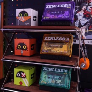 May include: A three-tiered display shelf holds several colorful items. On the top shelf are a white box with a cartoon face and a purple cassette tape case. The middle shelf has an orange box and a gold cassette tape case. The bottom shelf has a green box and a teal cassette tape case.