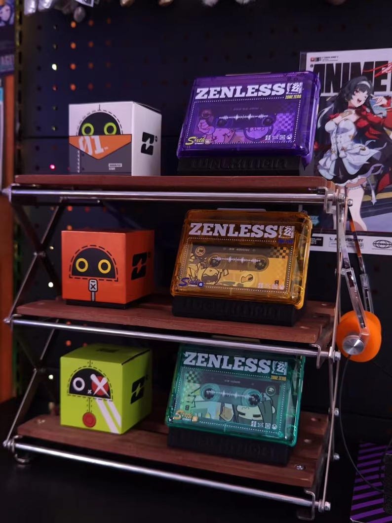 May include: A three-tiered display shelf holds several colorful items. On the top shelf are a white box with a cartoon face and a purple cassette tape case. The middle shelf has an orange box and a gold cassette tape case. The bottom shelf has a green box and a teal cassette tape case.