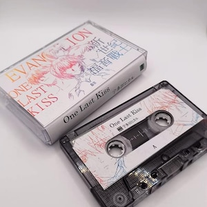 May include: A cassette tape with a clear plastic case. The cassette label and case feature the text "EVANGELION ONE LAST KISS" in English and Japanese. The cassette tape is black with a white label and a colorful design.