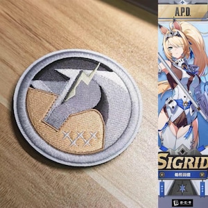 Op de afbeelding: Een ronde geborduurde patch met een gestileerd geometrisch ontwerp in grijs en beige, een centrale bliksemschichtvorm en drie kleine kruissteekaccenten. De patch heeft een dikke grijze rand en wordt getoond naast een karakterillustratie.
