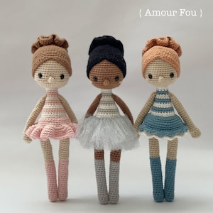 May include: Three crocheted ballerina dolls with different skin tones and hair colors. The dolls are wearing tutus and have different colored socks. The dolls are standing in a row on a white background. The text "Amour Fou" is written above the dolls.