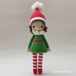 May include: A crocheted elf doll with brown hair, a green dress, red and white striped stockings, and a red and white Santa hat with a white pom-pom.