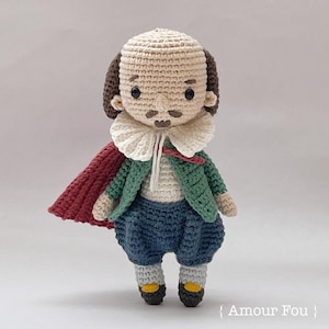 Puede incluir: Muñeco de crochet de un hombre que lleva una chaqueta verde, una capa roja, un cuello blanco y pantalones azules. El muñeco tiene el pelo castaño, un bigote y una barba.