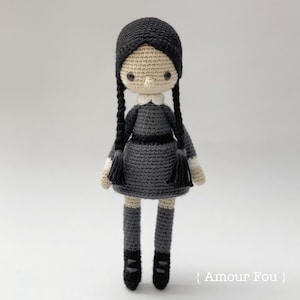 May include: A crocheted doll with black hair, a gray dress, and black shoes. The doll has a white collar and a sweet expression.