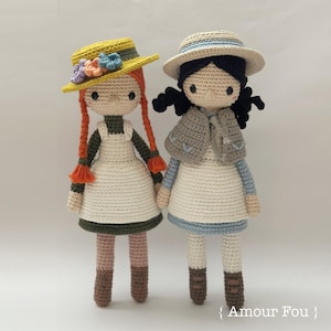 May include: Two crocheted dolls with long hair, wearing dresses and hats. The doll on the left has red hair and a yellow hat with flowers. The doll on the right has black hair and a straw hat. Both dolls are wearing brown shoes.