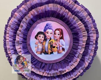 Może przedstawiać: Okrągła, warstwowa piñata w odcieniach fioletu i różu. Środek przedstawia okrągły obraz trzech animowanych postaci. Piñata ma pofałdowaną konstrukcję z bibuły, z błyszczącą obwódką wokół centralnego obrazu.