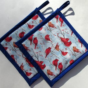 May include: Two blue and white pot holders with a wintery cardinal design. The pot holders have a blue trim and a loop for hanging.
