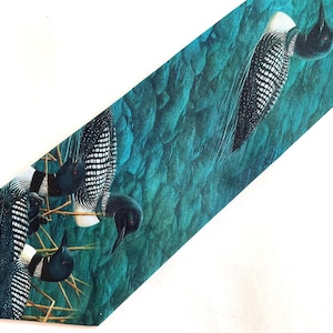 May include: A teal necktie featuring a pattern of loons. The birds are depicted with black heads, white and black speckled wings, and white markings. The background is a textured teal color, resembling water.