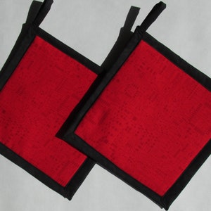 May include: Two red and black pot holders with a geometric pattern. The pot holders have black fabric trim and a loop for hanging.