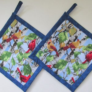 May include: Two blue-trimmed pot holders with a wintery design featuring red cardinals and birch trees on a blue background.