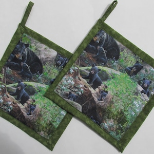 May include: Two green fabric pot holders with a black bear and cubs print. The pot holders have a loop for hanging.