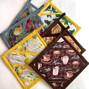 May include: Four square fabric pot holders with hanging loops. One features red cardinals on branches with gray trim, one has lemons and text with yellow trim, one shows blueberries and leaves with yellow trim, and one displays coffee drinks with brown trim.