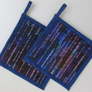 May include: Two square pot holders with a blue border and a digital code pattern in shades of blue, purple, and white. Each pot holder has a loop for hanging.