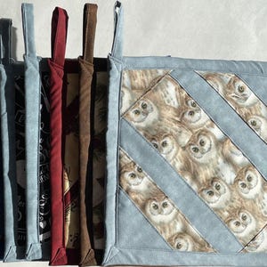 May include: Set of 10 colourful pot holders with different patterns. The pot holders are made of fabric and have a loop handle. One pot holder features a pattern of owls on a blue background.