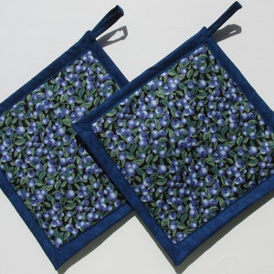 Peut inclure: Deux maniques de cuisine bleues et noires avec un motif de myrtilles. Les maniques ont une bordure bleu foncé et une boucle pour les accrocher.
