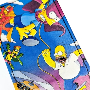 May include: A rectangular item with a vibrant blue background featuring cartoon characters. The design includes yellow, purple, and red figures in dynamic poses, with black stitching along the edges. The overall theme is a pop culture design.