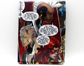 May include: A comic book cover featuring Storm, a superhero with white hair and blue skin, and other characters. The text on the cover reads "SHOULDN'T WE MAYBE TAKE THIS OPPORTUNITY TO...GET THE HELL OUT OF HELL?" and "NO. THIS IS STILL OUR FIGHT. WE WOULDN'T BE HERE IF IT WASN'T. WE HAVE TO FIND THE REST OF THE X-MEN."