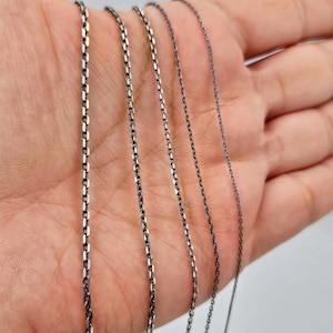May include: Five silver chains of varying lengths and thicknesses, displayed on a hand.