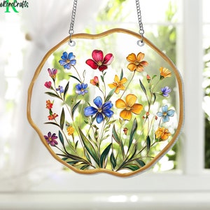 May include: A round stained glass suncatcher with a floral design. The suncatcher features a variety of colorful flowers, including red, yellow, blue, and purple. The flowers are surrounded by green leaves and are set against a clear glass background. The suncatcher is suspended from a silver chain.