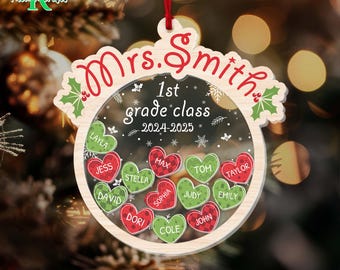May include: A wooden Christmas ornament with the text "Mrs. Smith 1st grade class 2024-2025". The ornament features a clear center with heart-shaped name tags. Names include Layla, Jess, David, Stella, Max, Sophia, Tom, Taylor, Judy, Emily, Dori, Cole, and John.