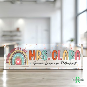 May include: A clear acrylic desk sign with a rainbow design and the text "Everyone Deserves a Voice". The sign also includes the text "Mrs. Clara Speech Language Pathologist".