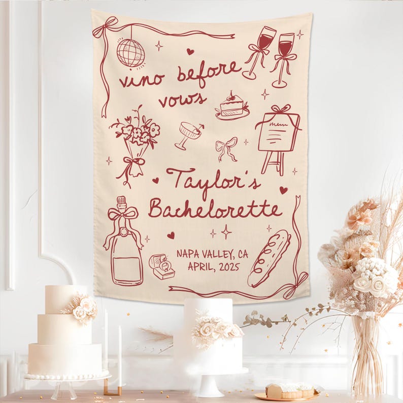 Op de afbeelding: Een cr&egrave;mekleurige stoffen wandhanger met donkerrode lijntekeningen van een discobal, wijnglazen, een boeket, een taart, een menu, een fles, een ringdoosje en een stokbrood met de tekst "vino before vows", "Taylor's Bachelorette" en "NAPA VALLEY, CA APRIL, 2025".