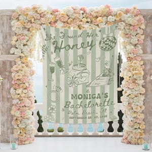 May include: A light green and white striped banner with the text "She Found Her Honey" and "Monica's Bachelorette Palm Beach, Fl September 25-27, 2025". The banner features illustrations of champagne glasses, a ring, and a jar of honey. The banner is surrounded by a floral arch.