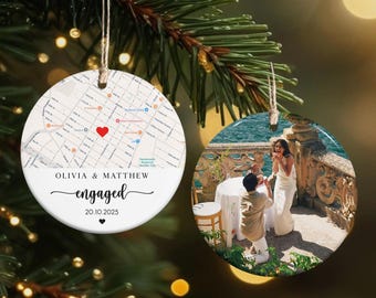 May include: Two round Christmas ornaments hanging from a pine branch. One ornament features a map with a red heart and the text "Olivia & Matthew engaged 20.10.2025". The other ornament shows a couple during a proposal.