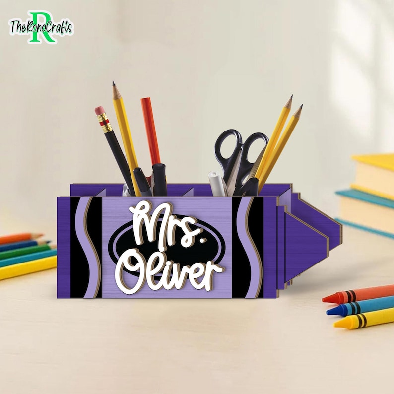 以下が含まれることがあります： 紫色のクレヨン型のデスクオーガナイザーで、白い文字で「Mrs. Oliver」と書かれています。オーガナイザーには鉛筆、ペン、ハサミが入っています。デザインには黒と金のアクセントが含まれています。「TheKonoCrafts」のロゴが左上にあります。