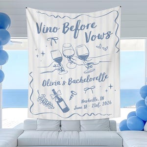 Puede incluir: Un tapiz de pared de tela blanca con rayas verticales azules y gr&aacute;ficos de arte lineal azul. Incluye el texto "Vino Before Vows", "Olivia's Bachelorette" y "Nashville, TN June 18 - 21st, 2026" junto a ilustraciones de copas de vino, una botella y uvas.