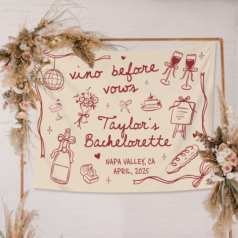Op de afbeelding: Een cr&egrave;mekleurige stoffen banner met donkerrode lijntekeningen van een discobal, champagneglazen, een boeket, een taart, een menu, een fles en een ringdoosje. De tekst luidt: vino before vows, Taylor's Bachelorette, NAPA VALLEY, CA, APRIL, 2025.