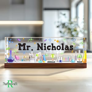 May include: A clear acrylic desk nameplate with a wooden base. The nameplate features a science theme with colourful beakers, test tubes, and a microscope. The name "Mr. Nicholas" is printed in black on the nameplate.