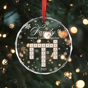 May include: A clear, round Christmas ornament with the word "Family" in elegant script and the phrase "Forever Linked Together." The ornament features a Scrabble-style design with names and the year 2025. It hangs from a red ribbon.