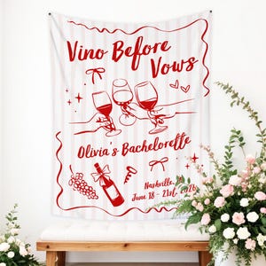 Puede incluir: Un tapiz de tela blanca con rayas verticales de color rosa claro, con ilustraciones rojas de copas de vino, una botella, uvas y lazos. El texto dice: Vino Before Vows, Olivia's Bachelorette, Nashville, June 18 - 21st, 2026.