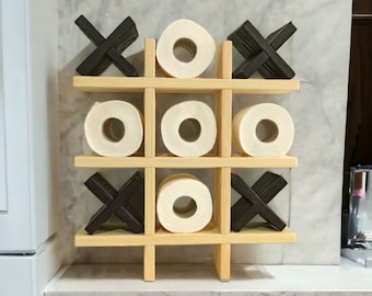 May include: A wooden tic-tac-toe game with black X's and O's made of toilet paper rolls. The game is on a shelf with a marble background.