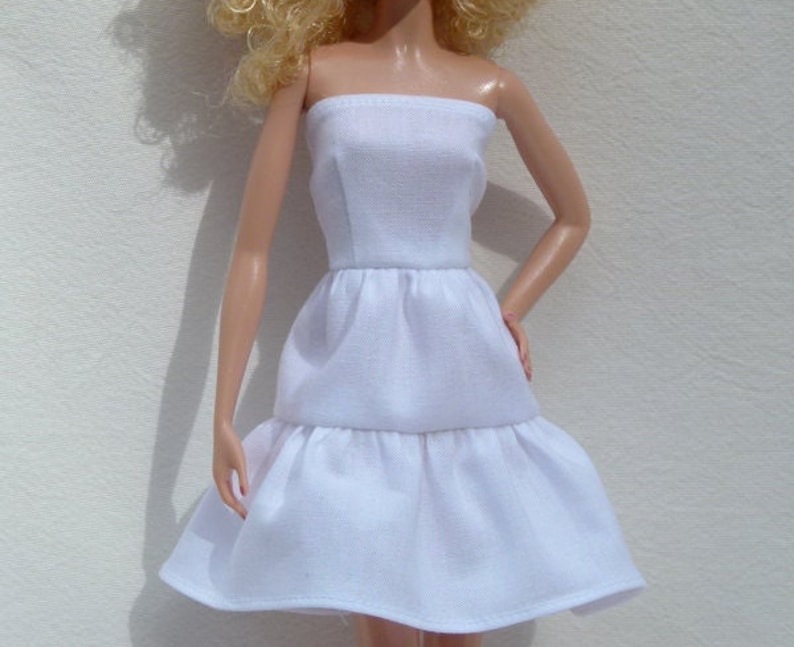 May include: A white strapless dress with a tiered skirt. The dress is made of a soft, lightweight fabric and has a simple, elegant design.
