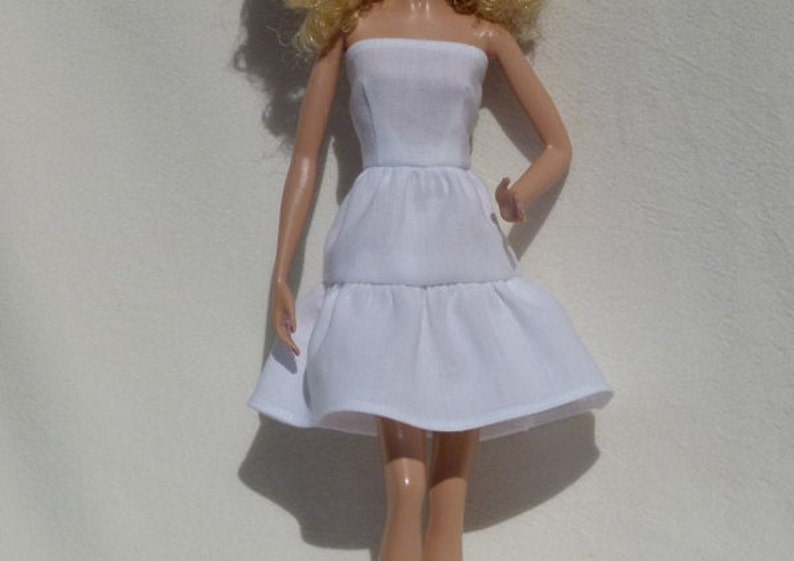 May include: A white strapless dress with a tiered skirt. The dress is made of a soft, flowing fabric.